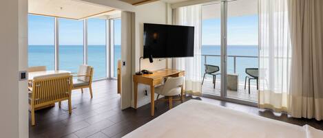 Habitación de hotel con una cama grande, un escritorio con silla, televisión y balcón con vista al mar.
