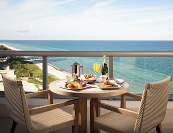 A pool area with lounge chairs and umbrellas, palm trees, and a view of the ocean at dusk. at Eden Roc Miami Beach
