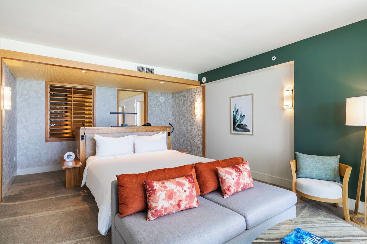 Una habitación de hotel con cama, sofá, sillón, escritorio y espejo.