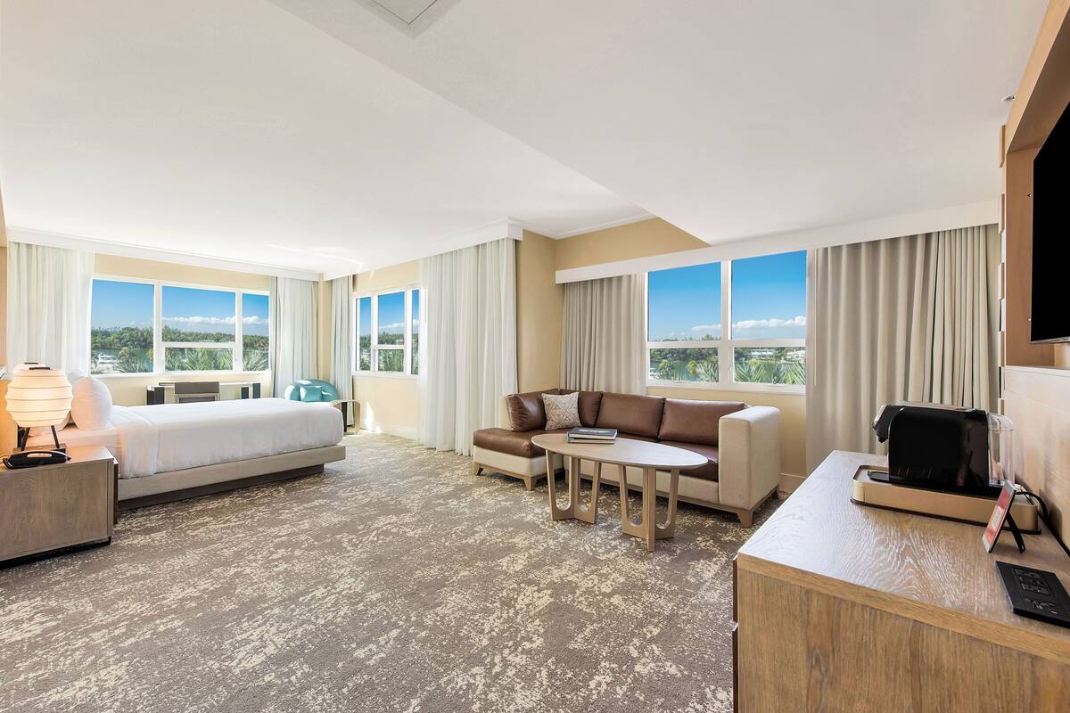 Una habitación de hotel con cama, sofá, mesa de centro y escritorio con televisor.