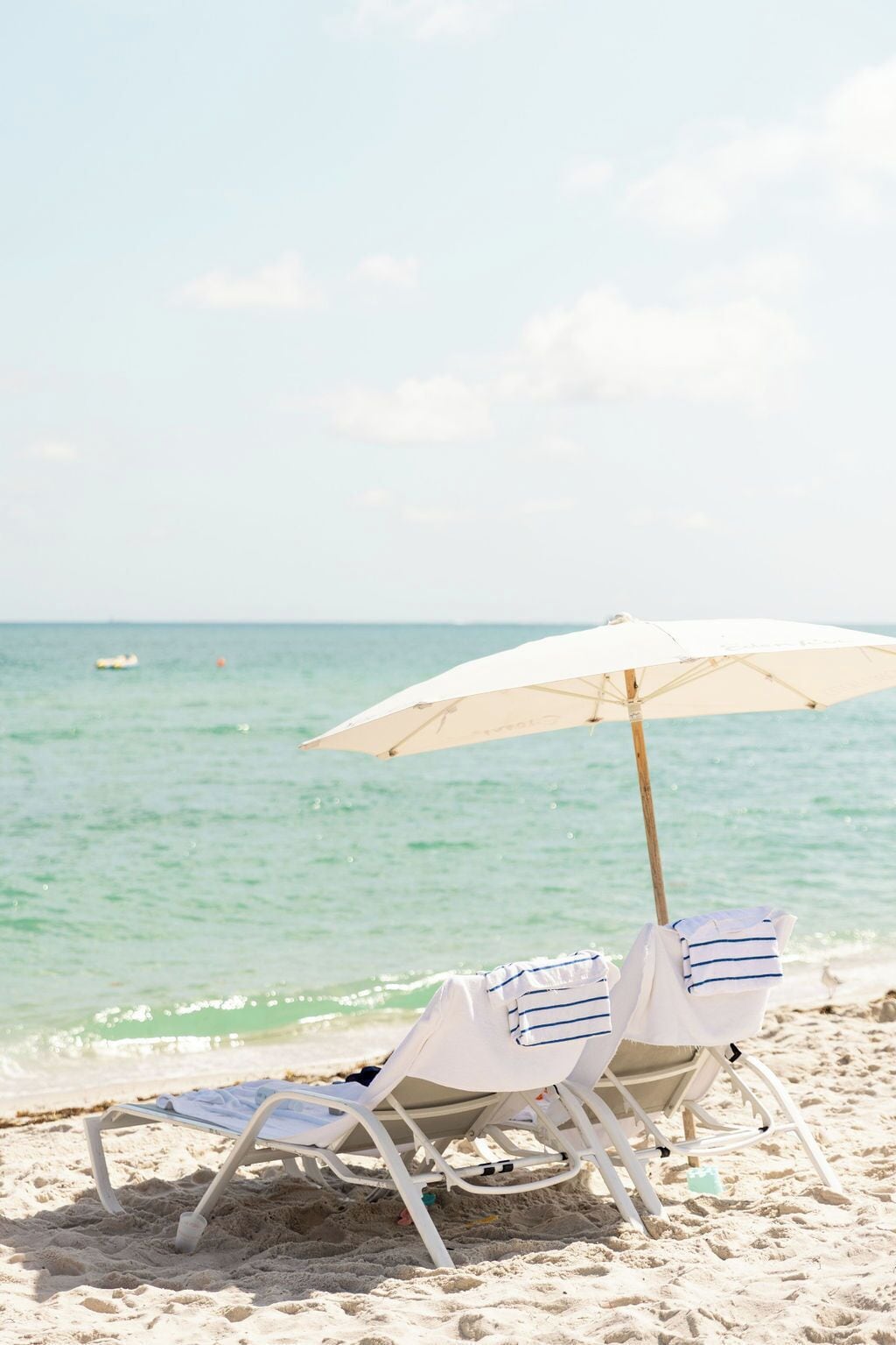 Two beach chairs under a white umbrella on a sandy beach with a calm sea in the background.