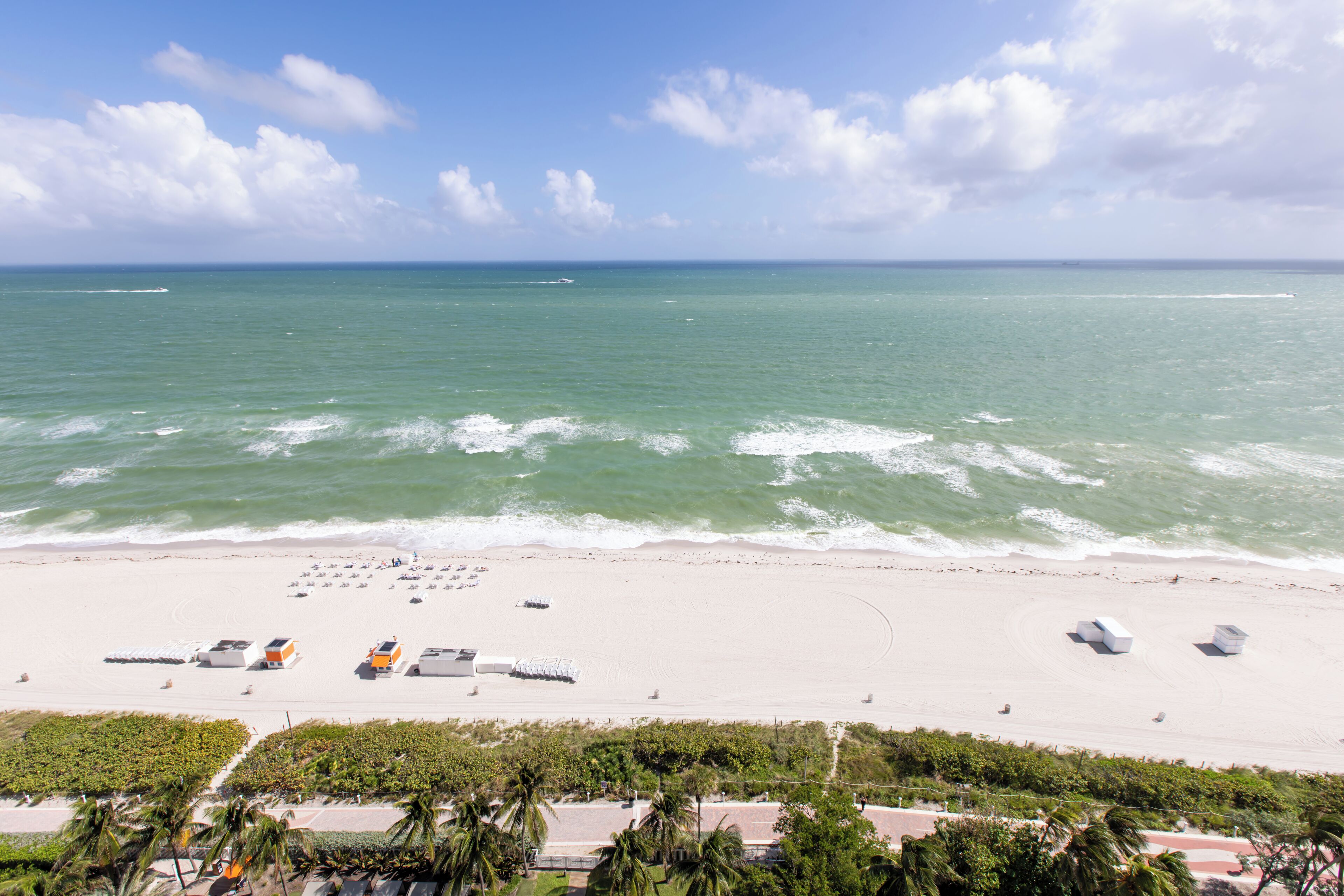 A beach with a clear sky, calm sea, and several beach umbrellas.
