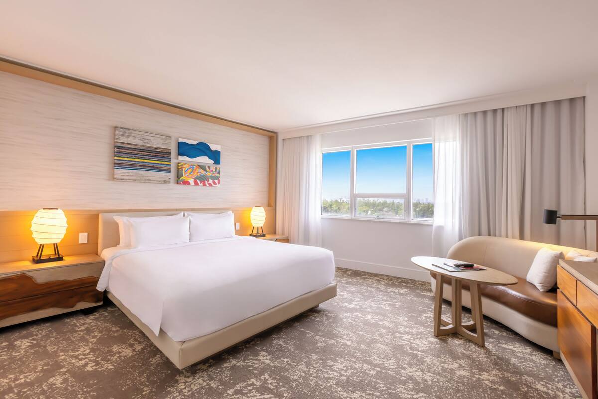 Una habitación de hotel con cama, sofá, una mesita y ventana con cortinas.