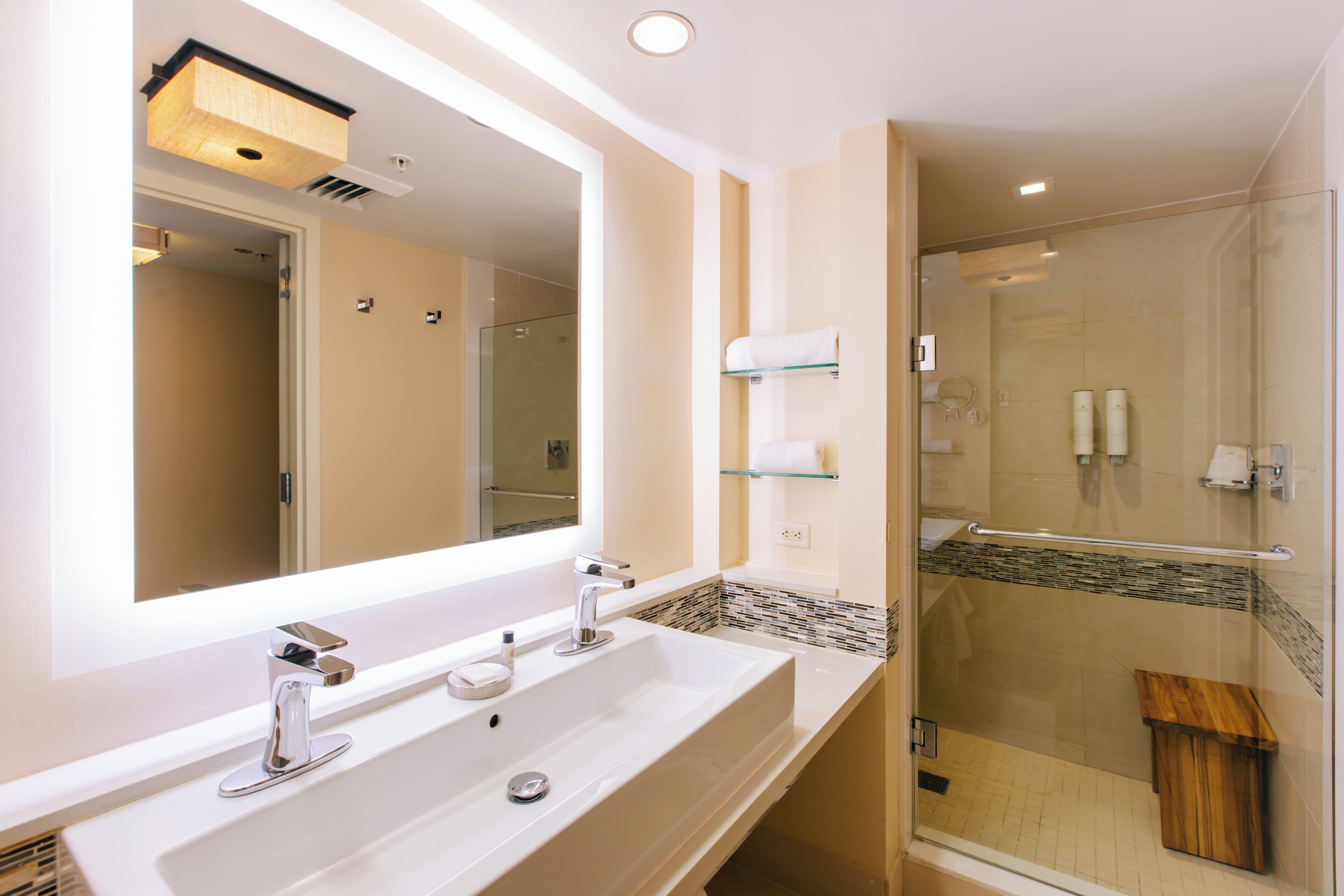 A modern bathroom with a large mirror, two sinks, and a glass-enclosed shower.