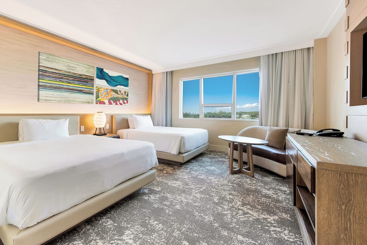 Habitación de hotel con dos camas, una mesita, un sofá, un televisor y obras de arte en la pared.