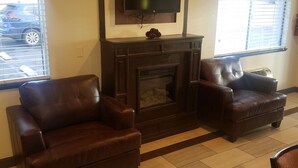 Un salon doté d’une cheminée, de deux fauteuils en cuir, d’un téléviseur fixé au-dessus de la cheminée et d’une fenêtre avec des stores.