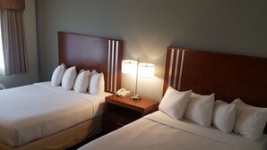 Deux lits doubles avec du linge de lit blanc, une tête de lit en bois à rayures verticales, une table de chevet avec une lampe et un téléphone.