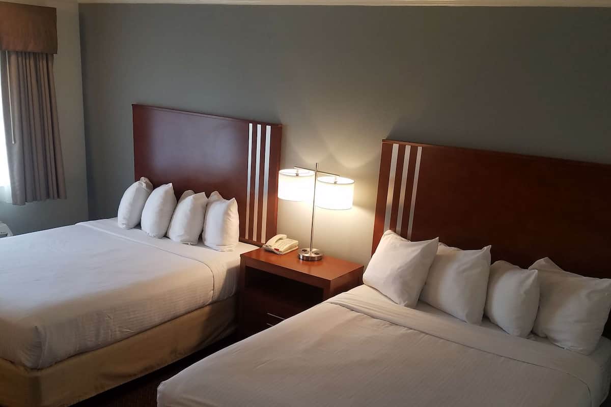 Two double beds with white linens, a wooden headboard with vertical stripes, a bedside table with a lamp, and a telephone.