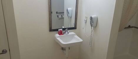 Un baño con lavamanos blanco, espejo, secador de pelo y zona de ducha.