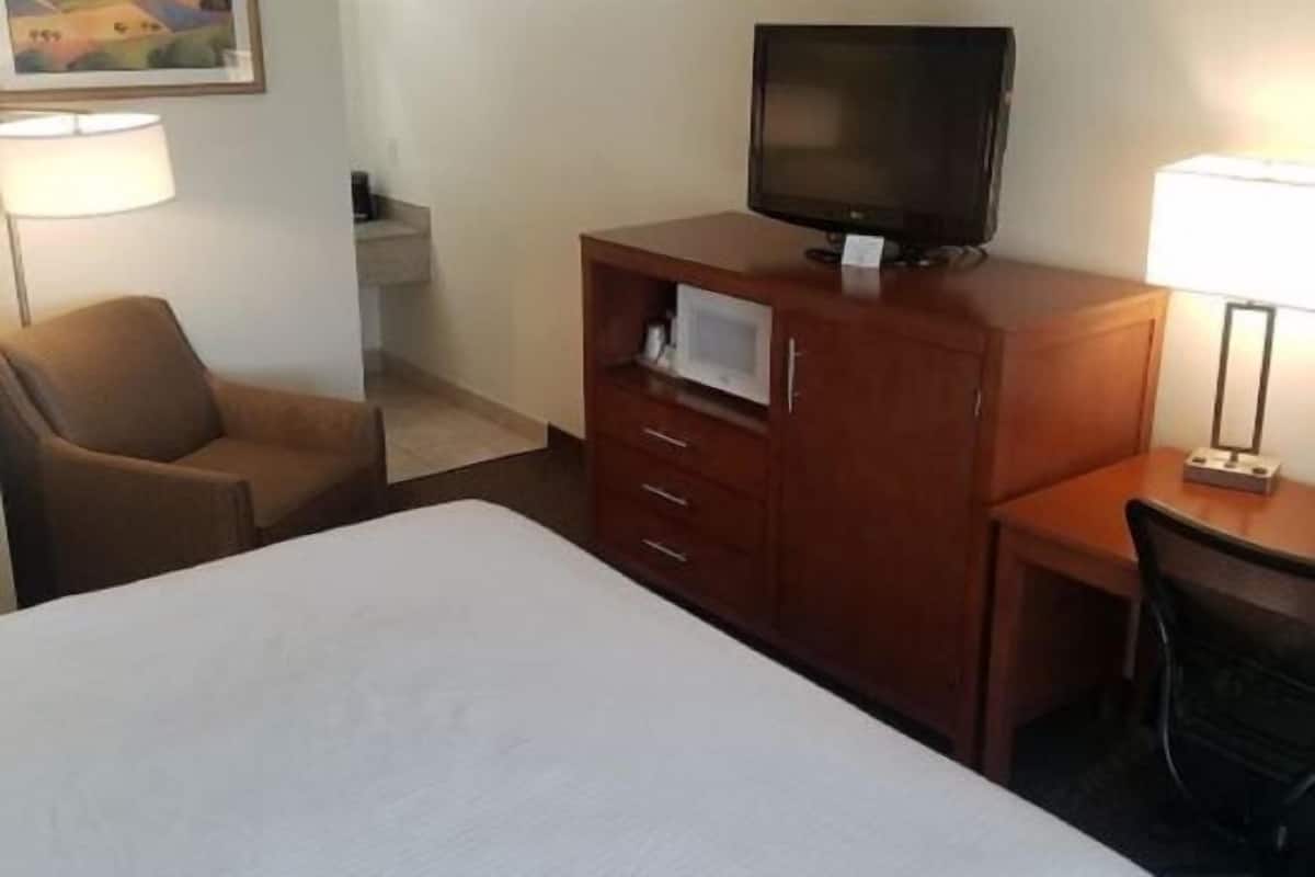A hotel room with a bed, a TV on a wooden cabinet, a desk, and a chair.