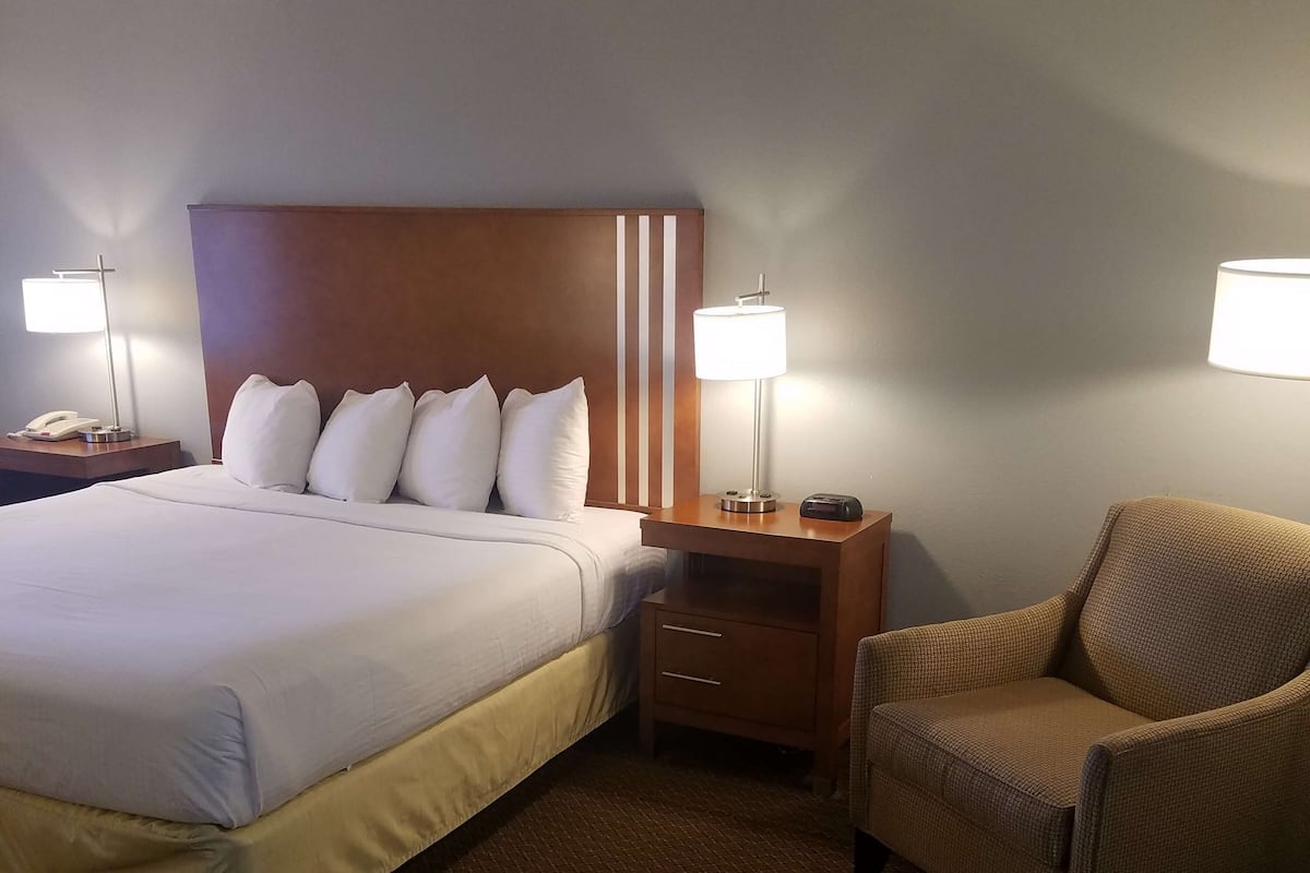 A hotel room with a large bed, two bedside tables with lamps, a chair, and a wooden headboard.