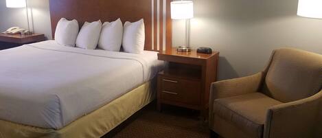 Una habitación de hotel con una cama grande, dos mesitas de noche con lámparas, una silla y un cabecero de madera.