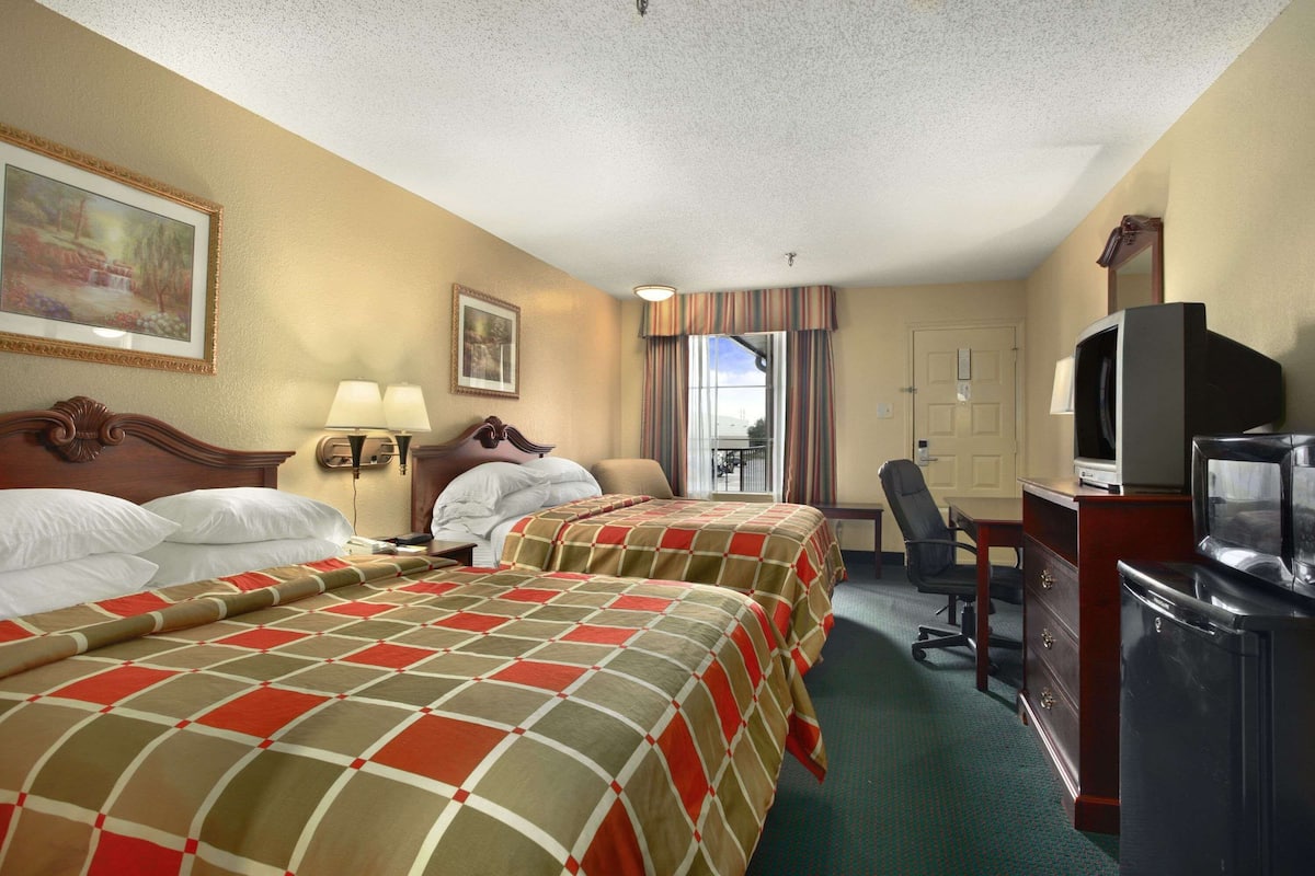 A hotel room with two beds, a desk with a television, a chair, and a window with curtains.