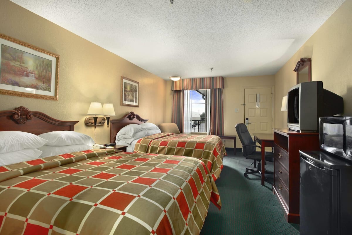 A hotel room with two beds, a desk with a television, a chair, and a window with curtains.