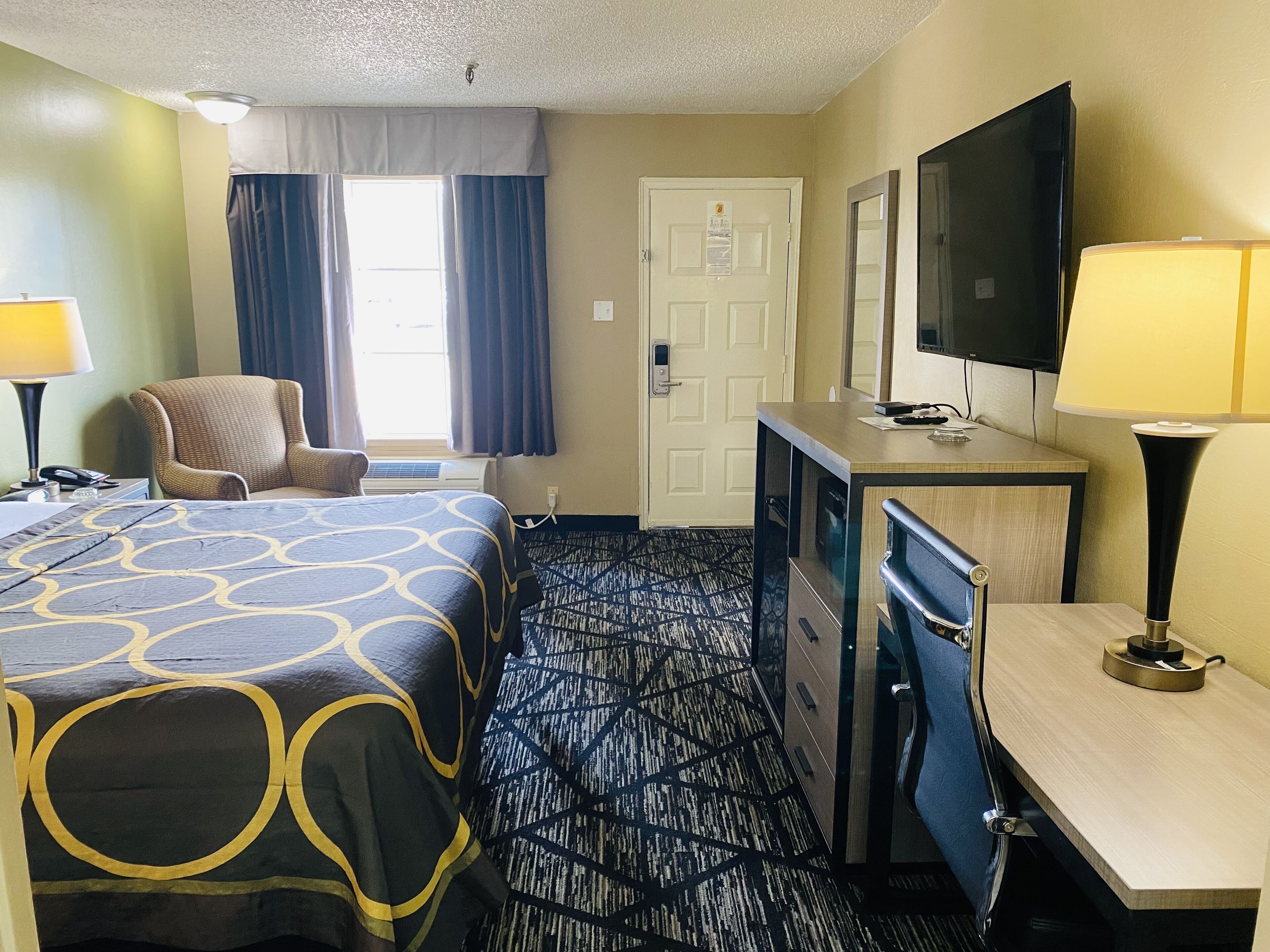 A hotel room with a bed, a desk, a chair, a television, and a window with curtains.