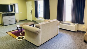 Une chambre meublée avec un canapé, un téléviseur posé sur un meuble, une petite table et une fenêtre avec des rideaux.