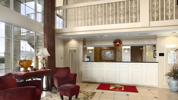 Un hall d’hôtel avec un comptoir d’accueil, des fauteuils à revêtement rouge, une grande fenêtre et un tapis décoratif.