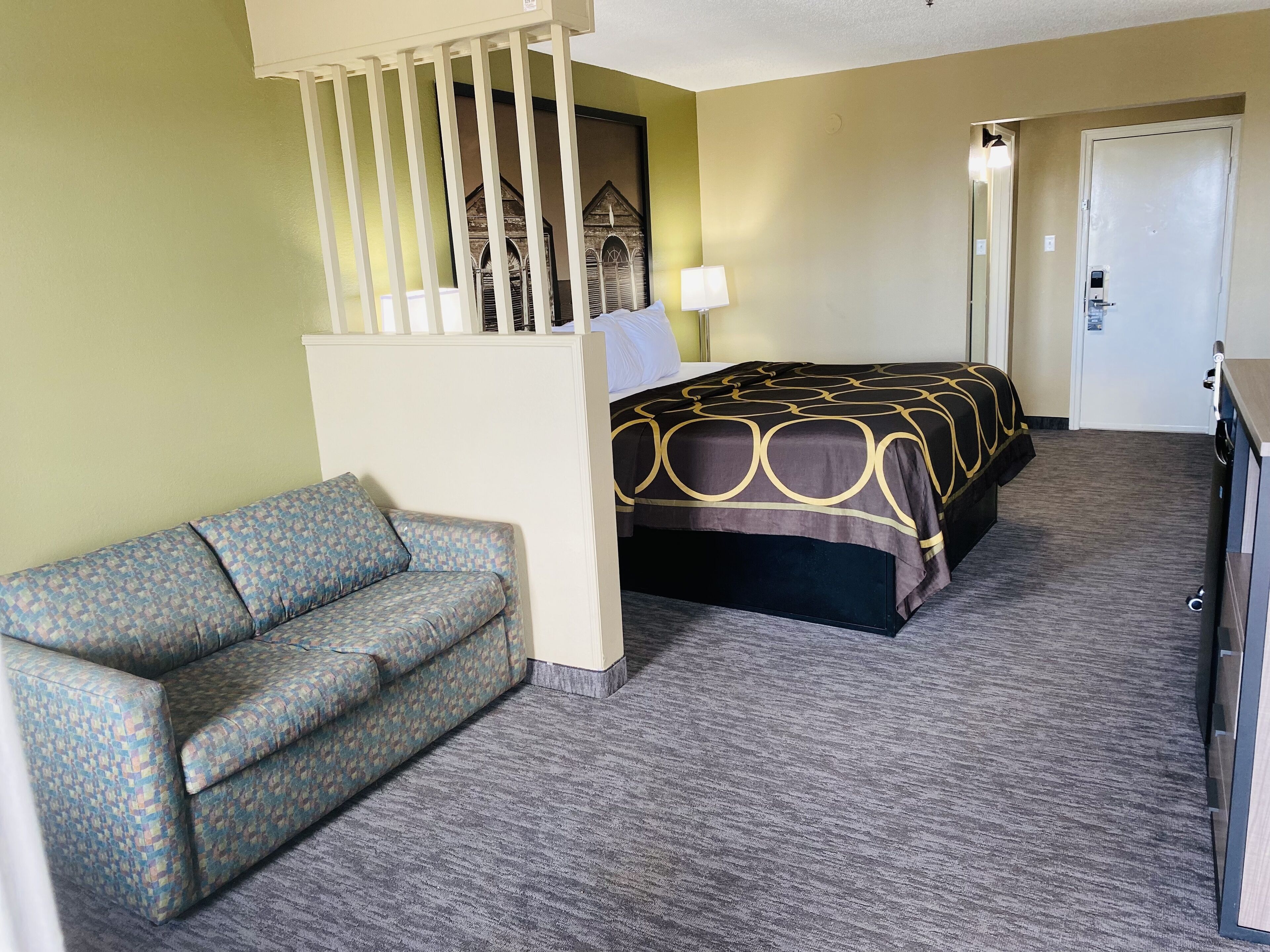 A hotel room with a bed, a sofa, a desk, and a door.