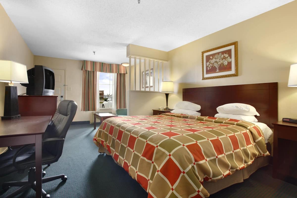 A hotel room with a bed, desk, chair, and a television on a stand.