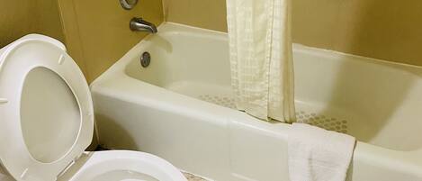 A bathroom with a toilet, a bathtub with a shower curtain, and a grab bar.