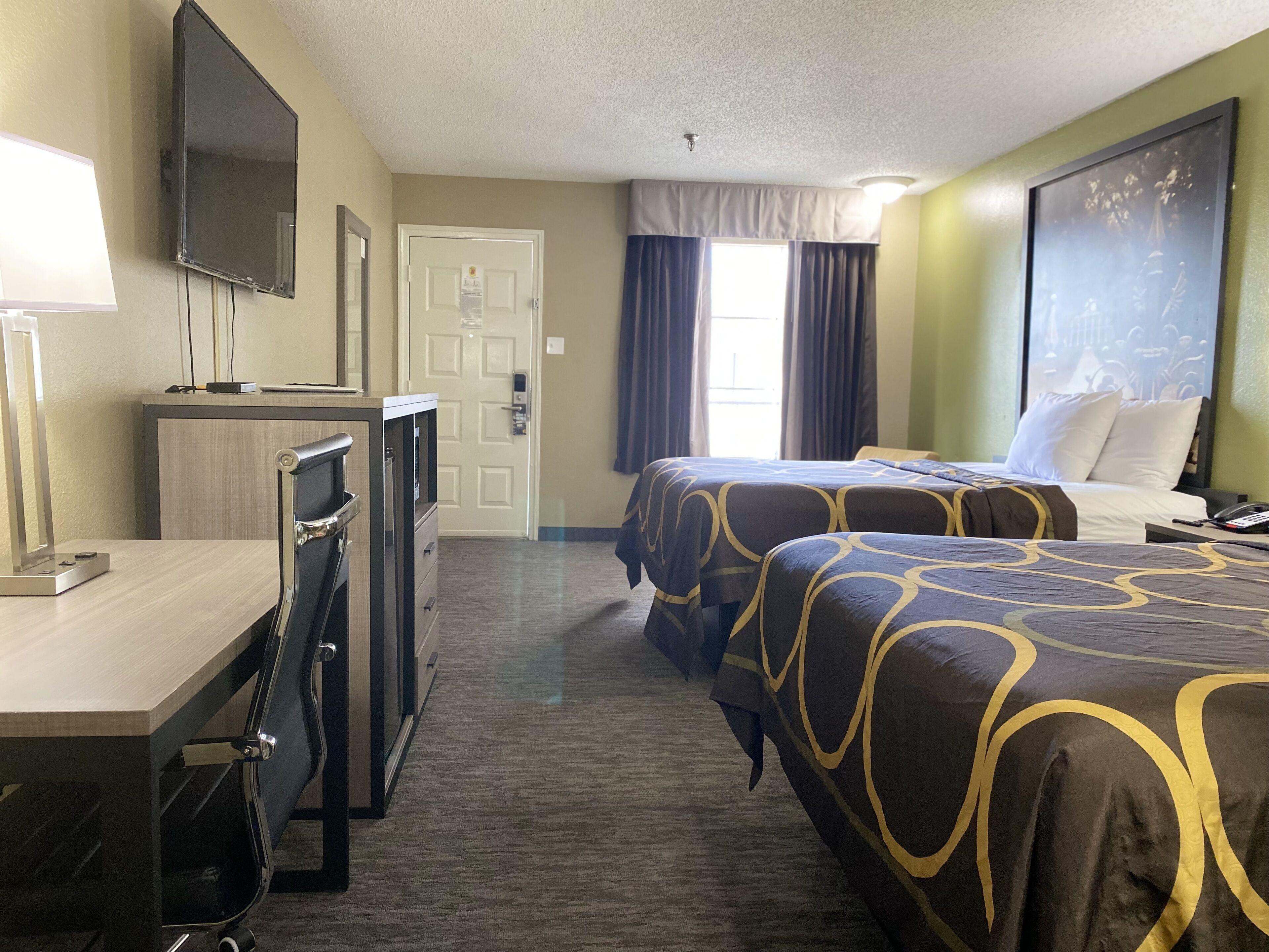 Habitación de hotel con dos camas, un escritorio, un televisor y una puerta.