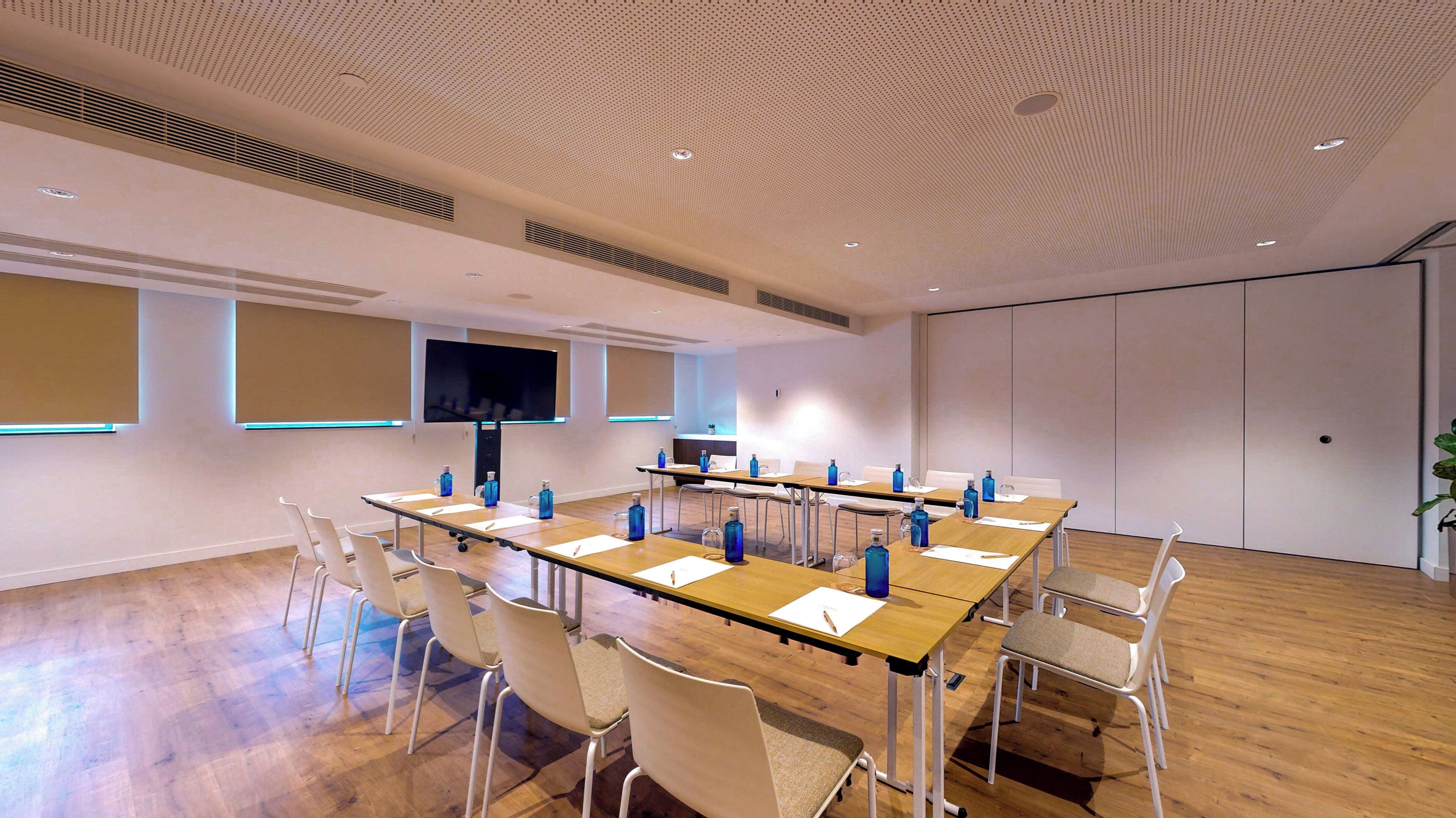 A conference room with a long table, chairs, a TV screen, and a plant.