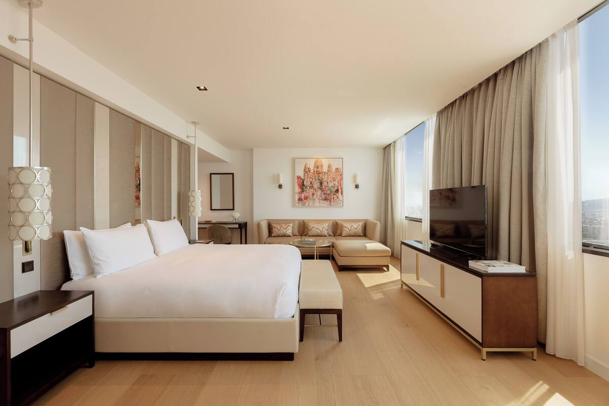 Una habitación de hotel moderna con una cama grande, un sofá, un televisor y un área de comedor.