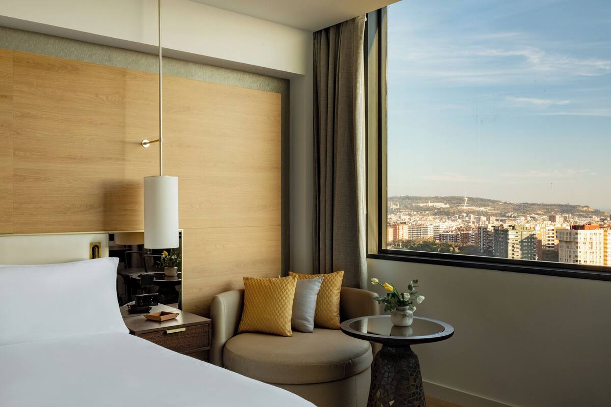 Una habitación de hotel con cama, sofá, mesa y vistas a un paisaje urbano.
