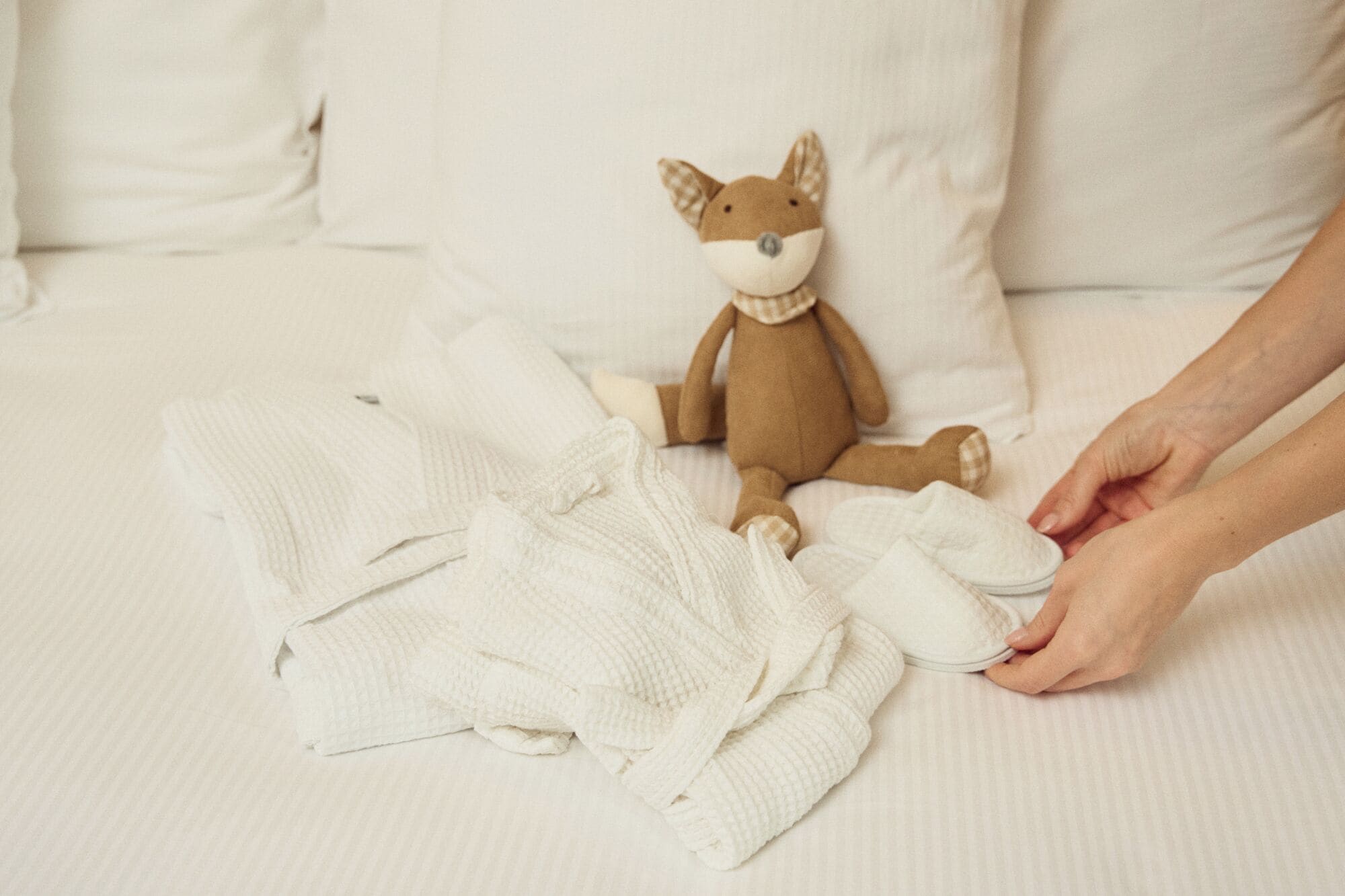 A person sitting on a bed with a plush toy and several folded white blankets.