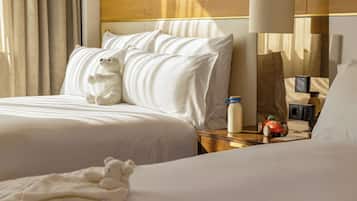 Ein Hotelzimmer mit einem Bett, Kissen, einem Teddybär, einem Nachttisch mit einer Flasche, einer Fernbedienung und einem Spielzeugauto.