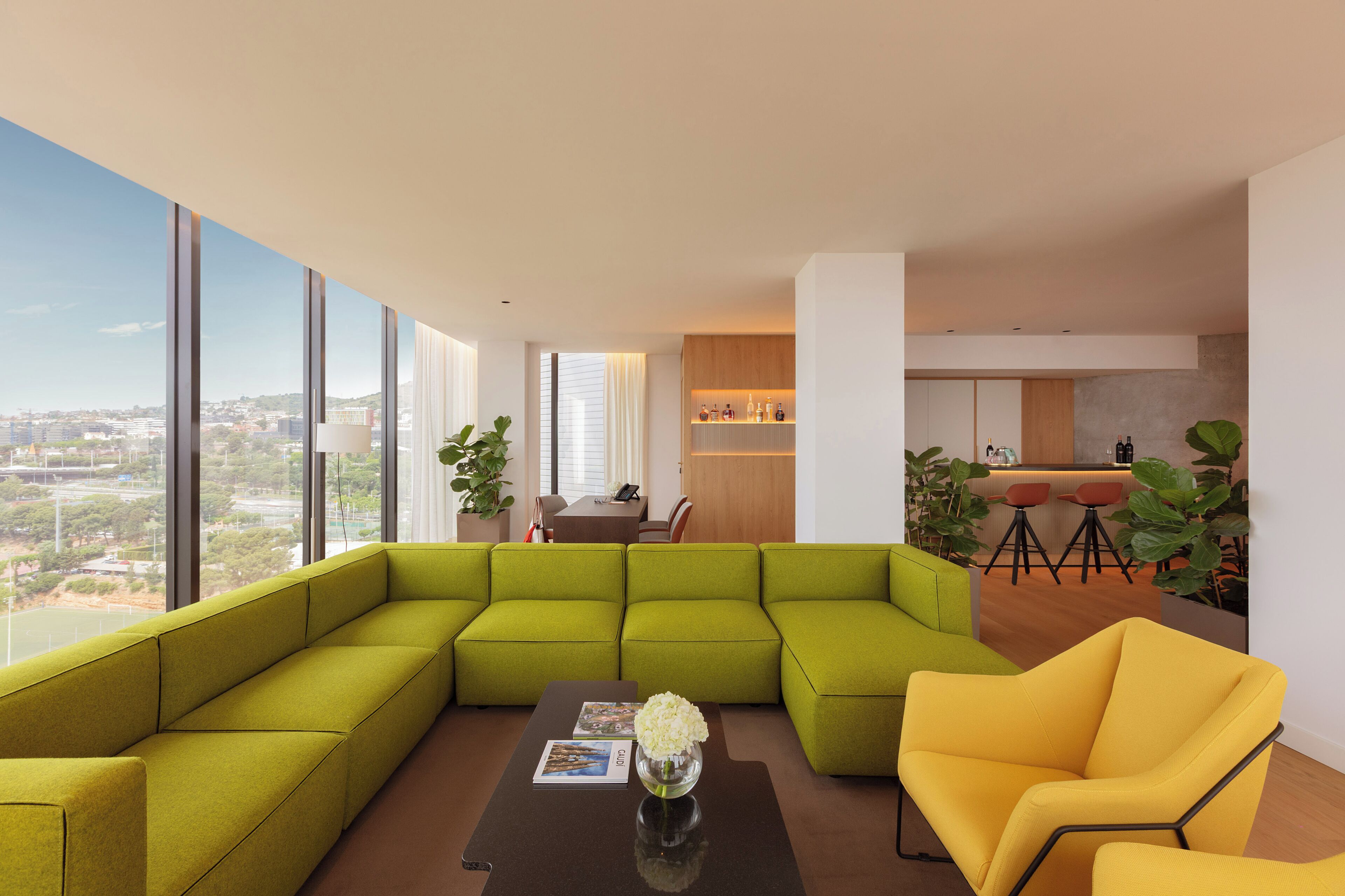 Una sala moderna con un sofá modular, un sillón amarillo y una mesa de centro con un florero.