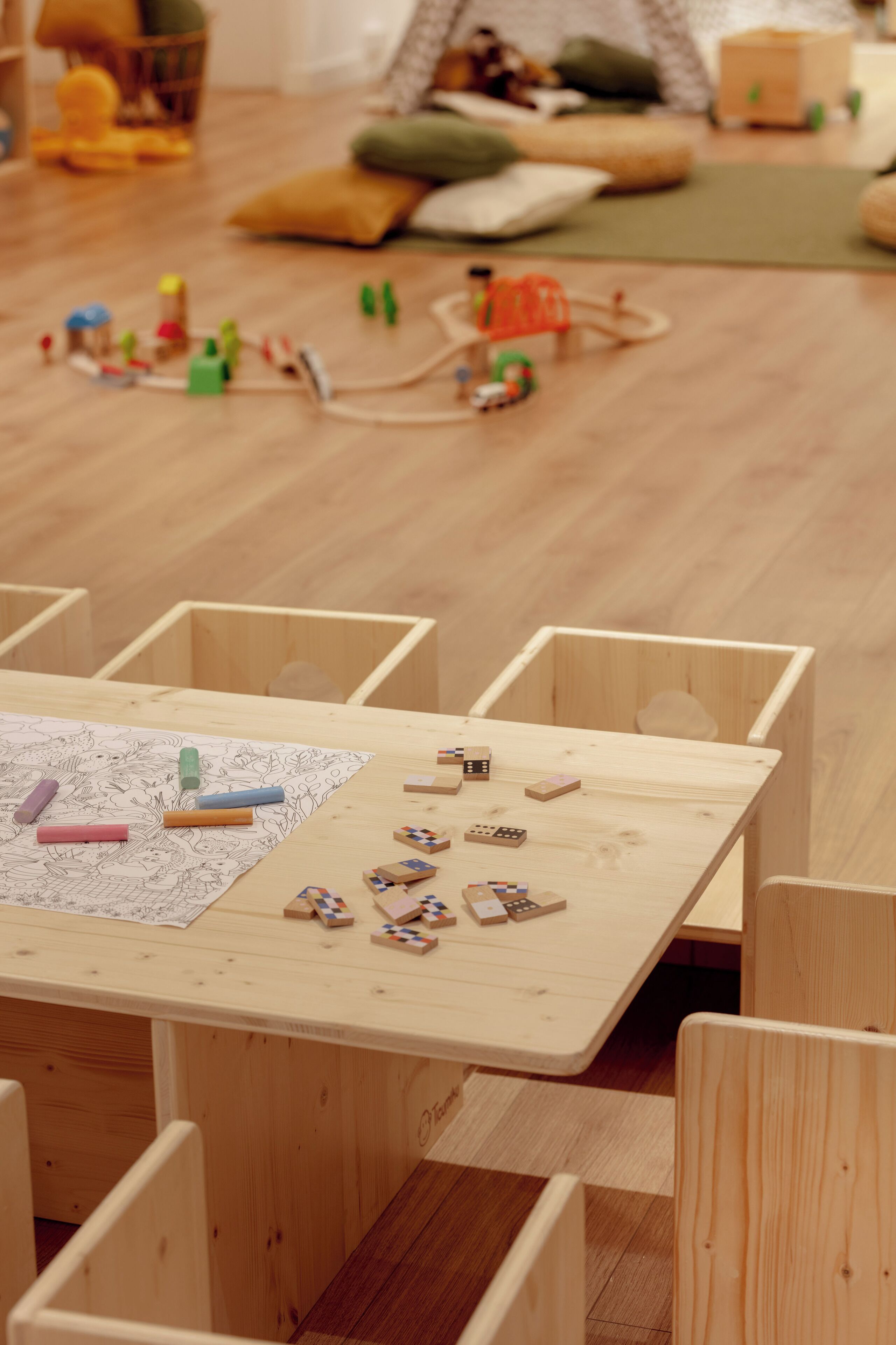 Una mesa de madera con un dibujo para colorear y piezas de un rompecabezas, rodeada de sillas de madera a juego.