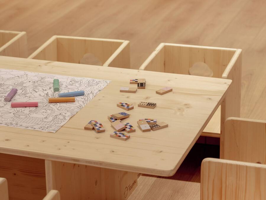Una mesa de madera con un dibujo para colorear y piezas de un rompecabezas, rodeada de sillas de madera a juego.