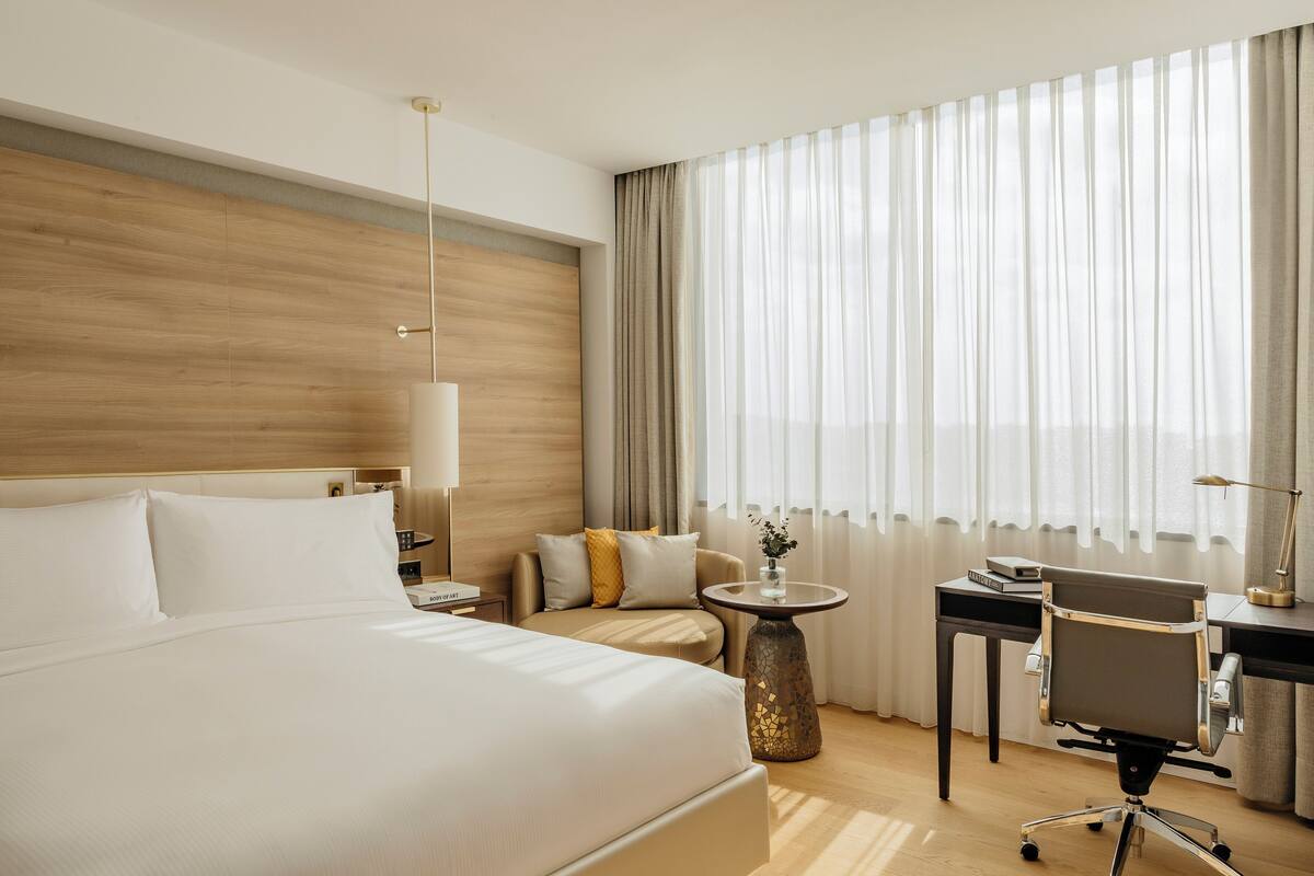 Una habitación de hotel con una cama grande, un escritorio, una silla y un ventanal con cortinas.