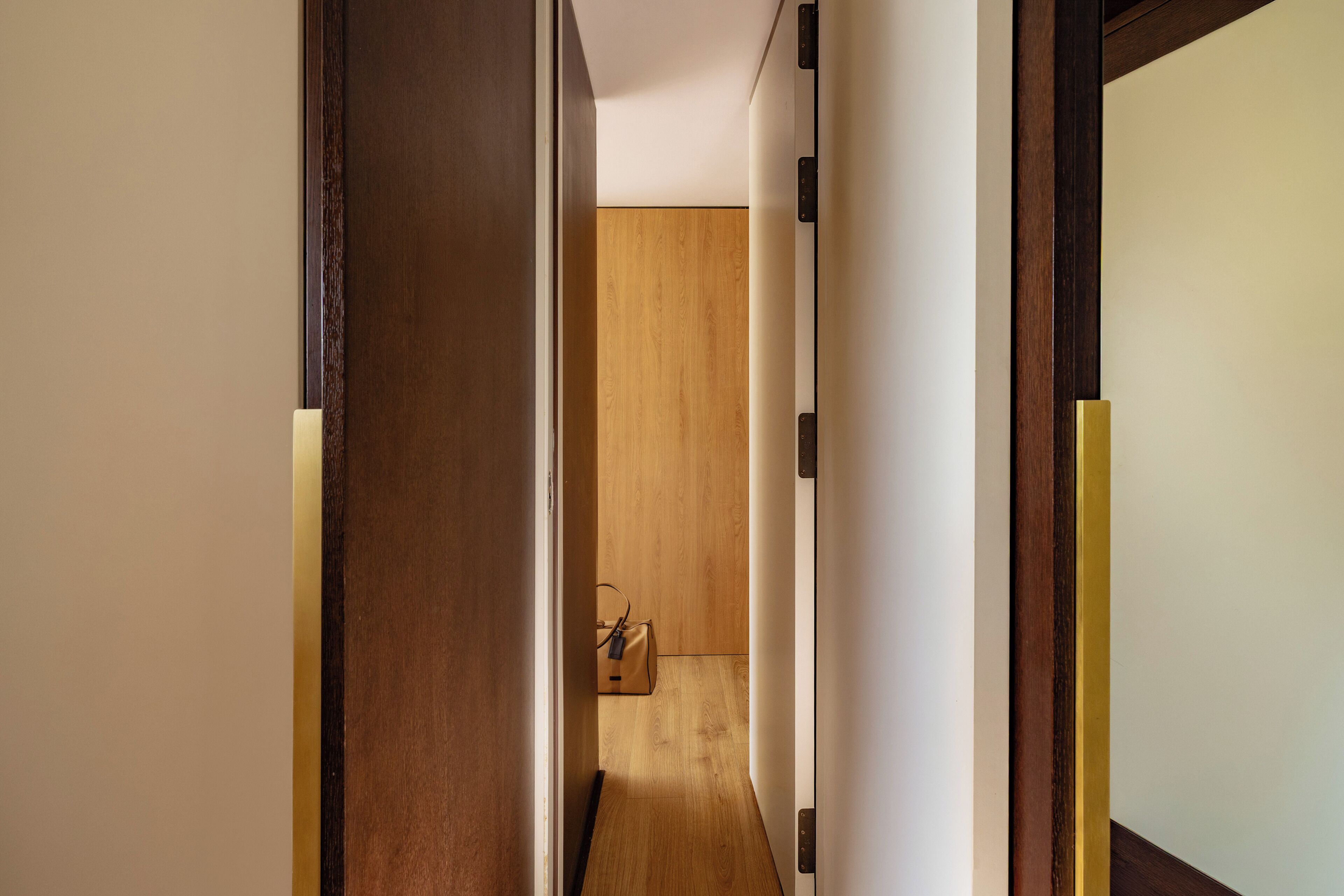 Un pasillo con puerta de madera, pared blanca y suelo de madera.