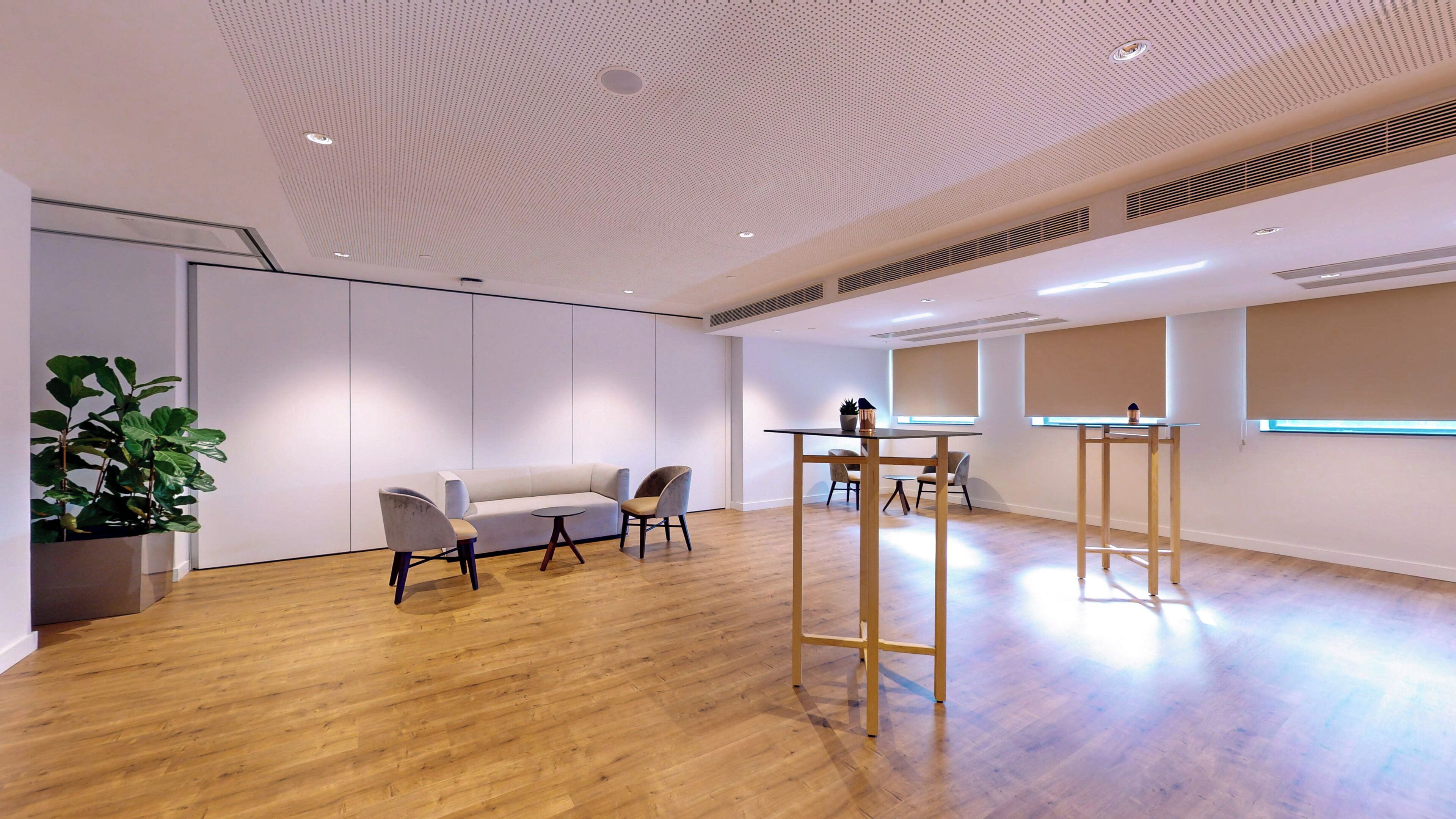 A spacious room with a wooden floor, a white sofa, two chairs, a small table, and a potted plant.