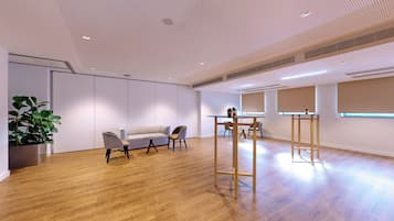 Una habitación amplia con suelo de madera, un sofá blanco, dos sillones, una mesita y una planta en maceta.