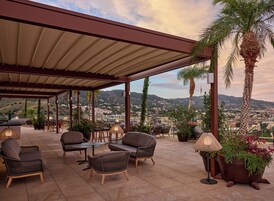 An outdoor patio with wicker furniture, a covered roof, and a view of a cityscape.