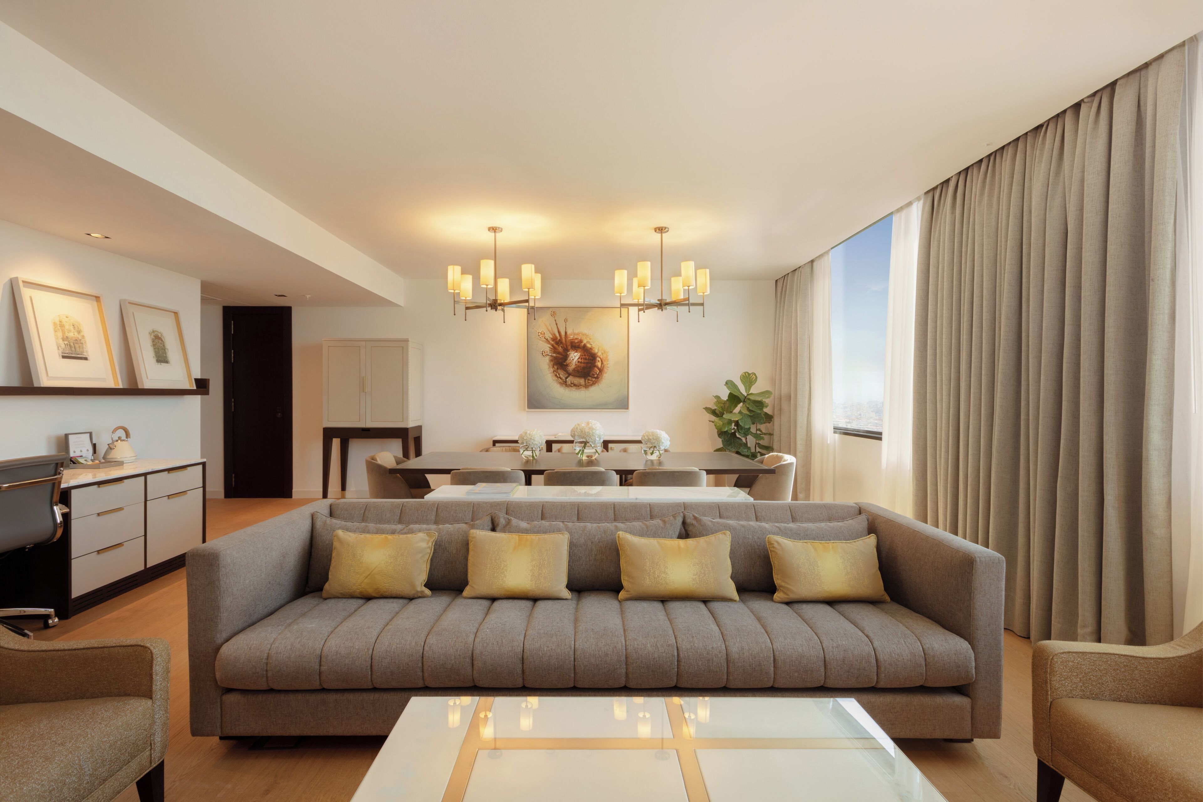 Ein modernes Wohnzimmer mit grauem Sofa, einem Esstisch und einer Pendelleuchte.
