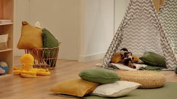 Una sala de juegos con piso de madera, una casita de juegos, un tipi y un juego de trenes de juguete.