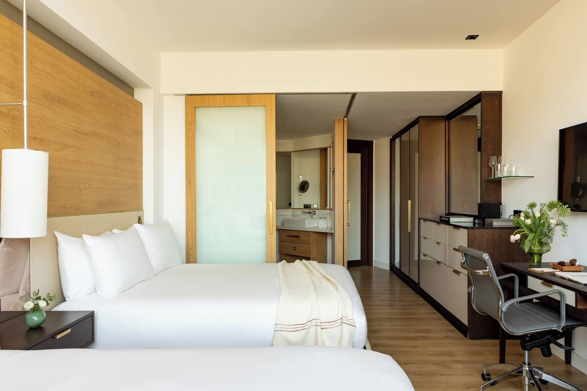 Habitación de hotel moderna con una cama grande, un escritorio, una silla, una mesita de noche, una lámpara y un florero con flores.