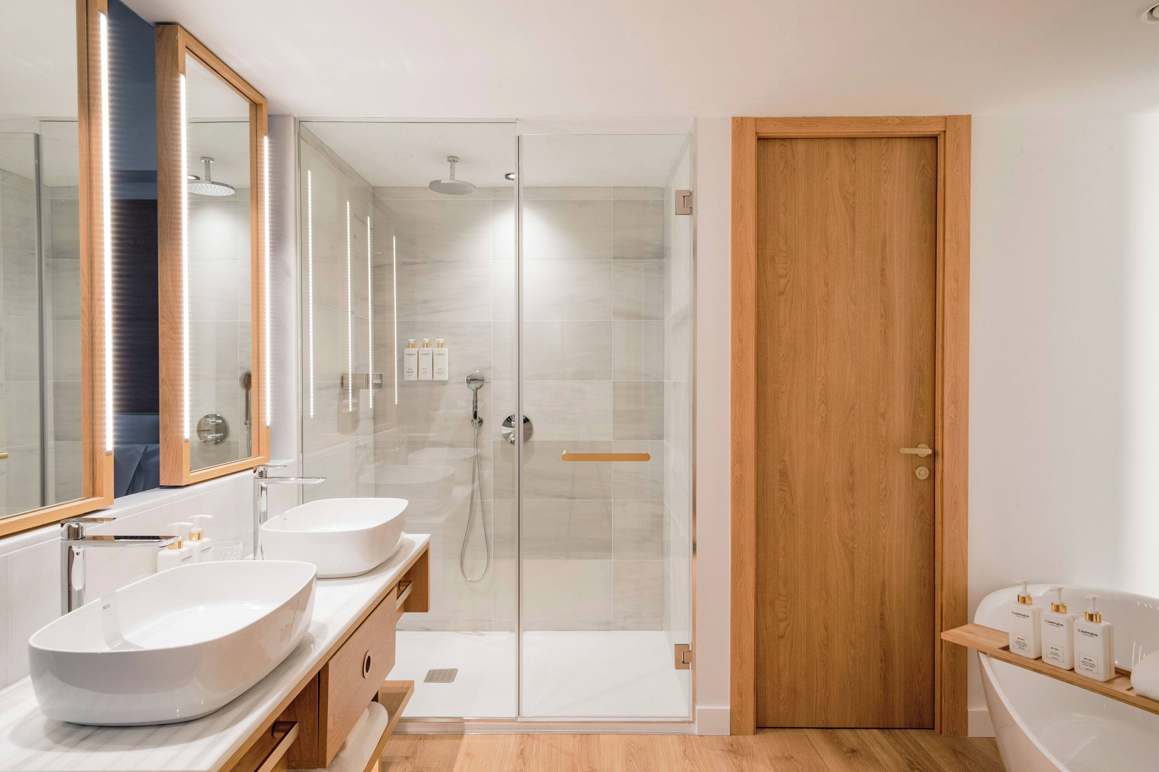 A modern bathroom with two sinks, a glass-enclosed shower, and a wooden door.