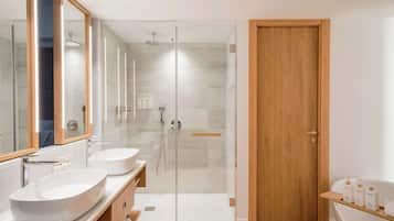 A modern bathroom with two sinks, a glass-enclosed shower, and a wooden door.