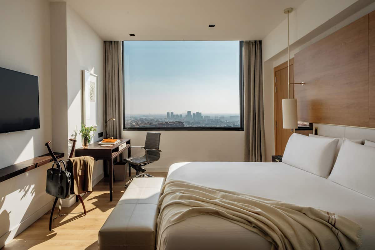 Habitación de hotel con una cama grande, un escritorio con silla, un televisor y vistas a la ciudad.