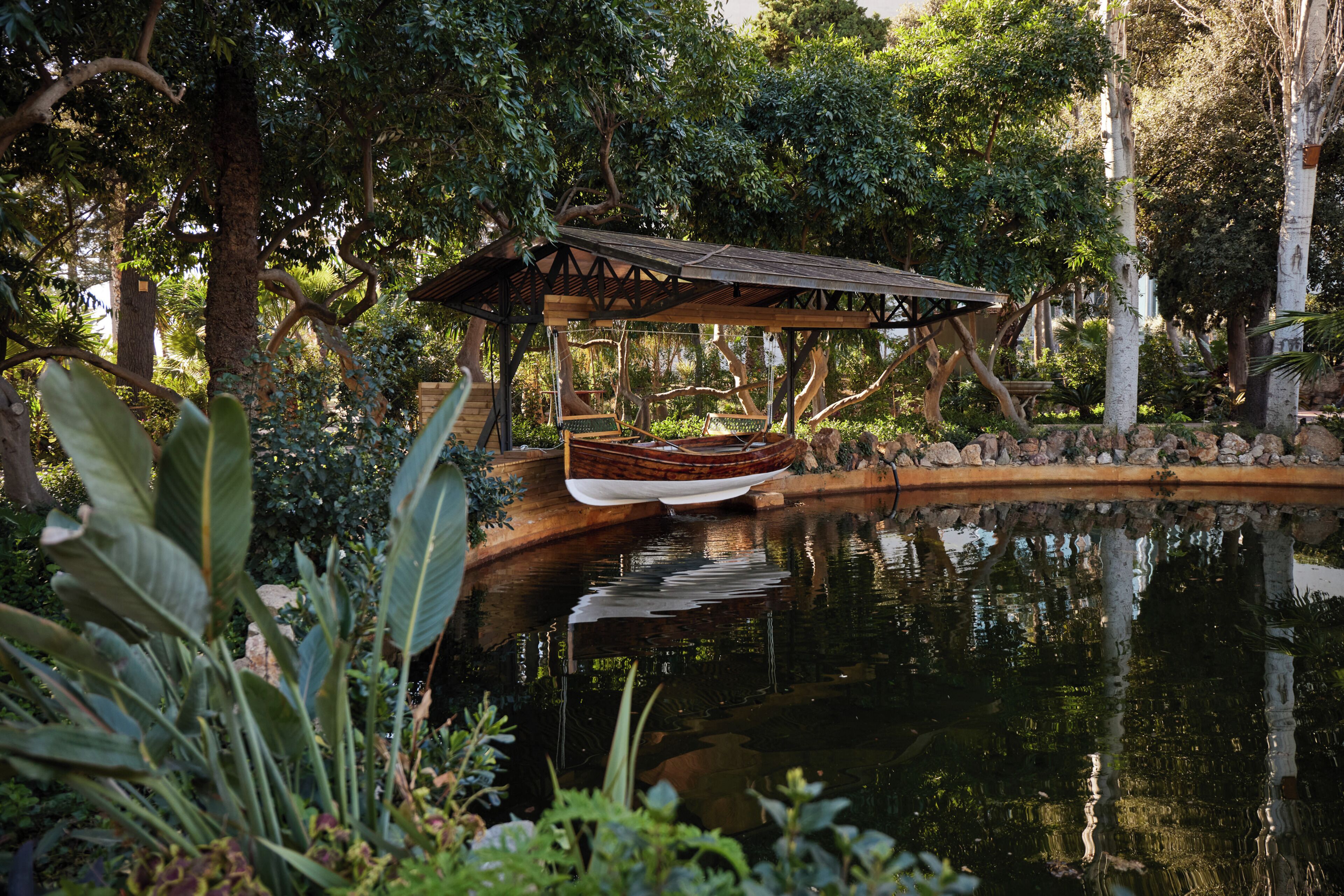 Un jardín tranquilo con un bote de madera en un estanque, rodeado de exuberante follaje y un pabellón de madera.