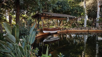 Un jardín tranquilo con un bote de madera en un estanque, rodeado de exuberante follaje y un pabellón de madera.