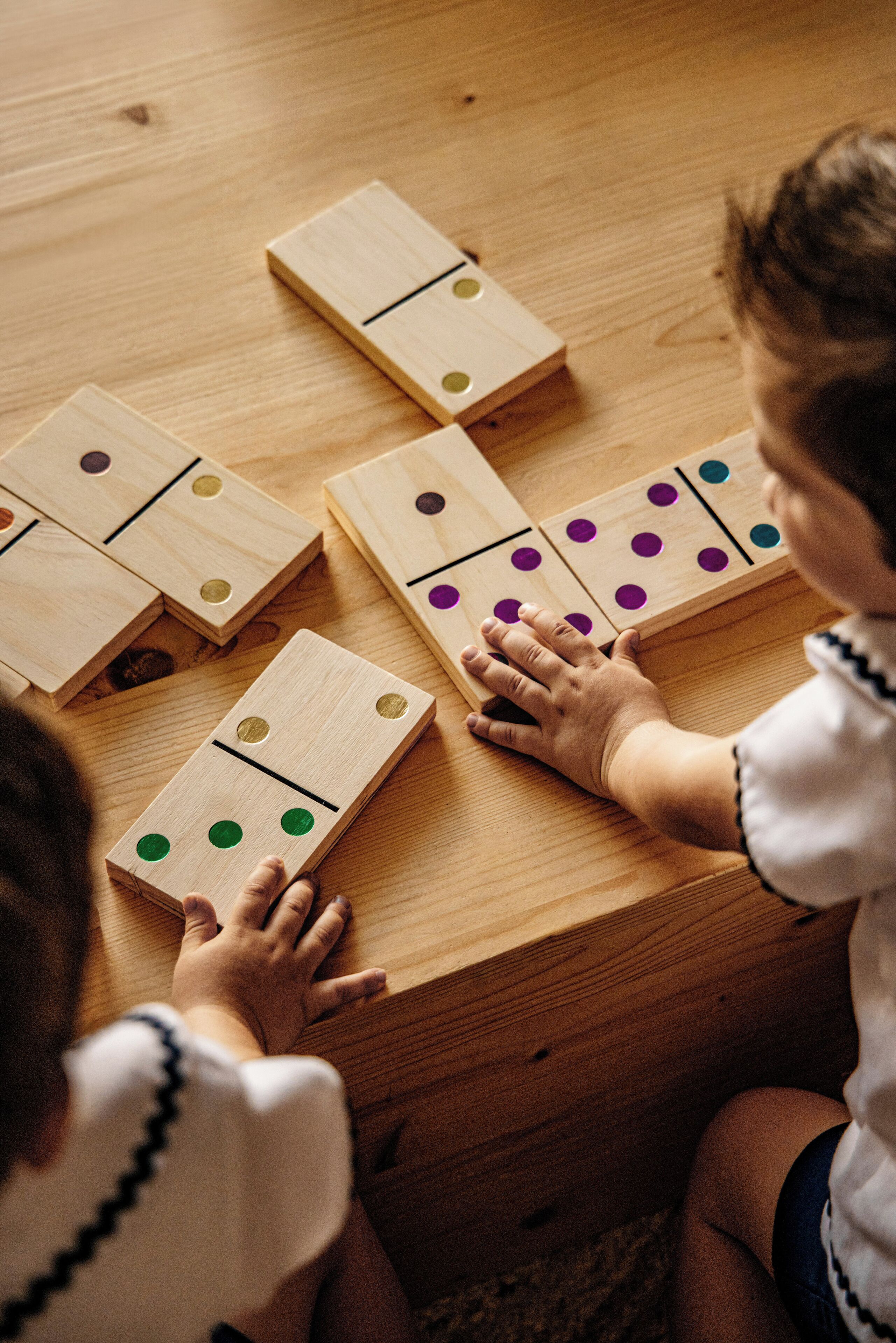Children playing with wooden dominoes on a wooden table.