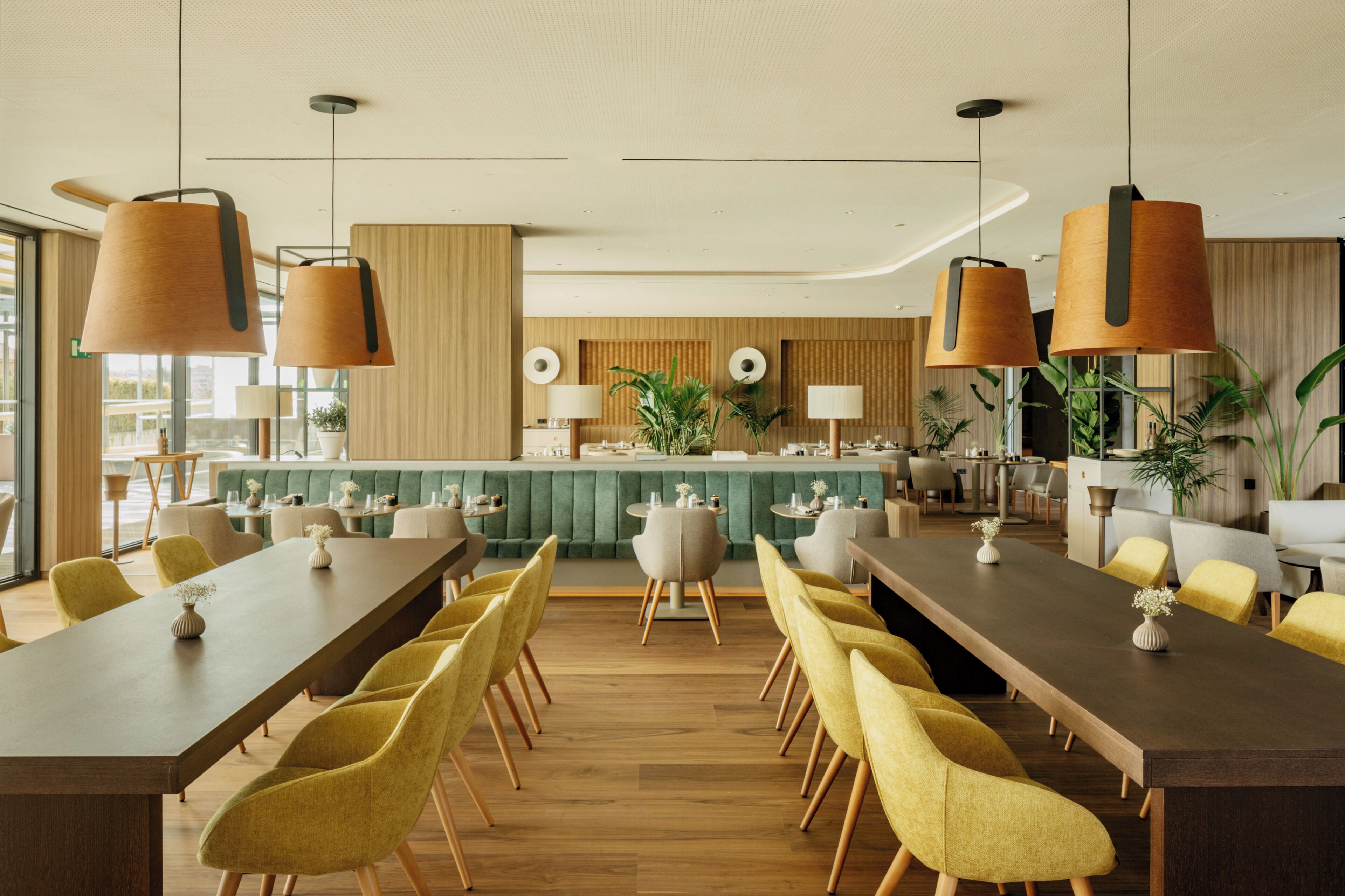 Een moderne hotellobby met een lange receptiebalie, gele stoelen en grote hanglampen.