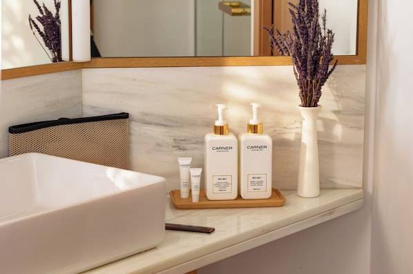 A bathroom vanity with a white sink, a mirror, and toiletries including two bottles of hand and body lotion and a small tube.