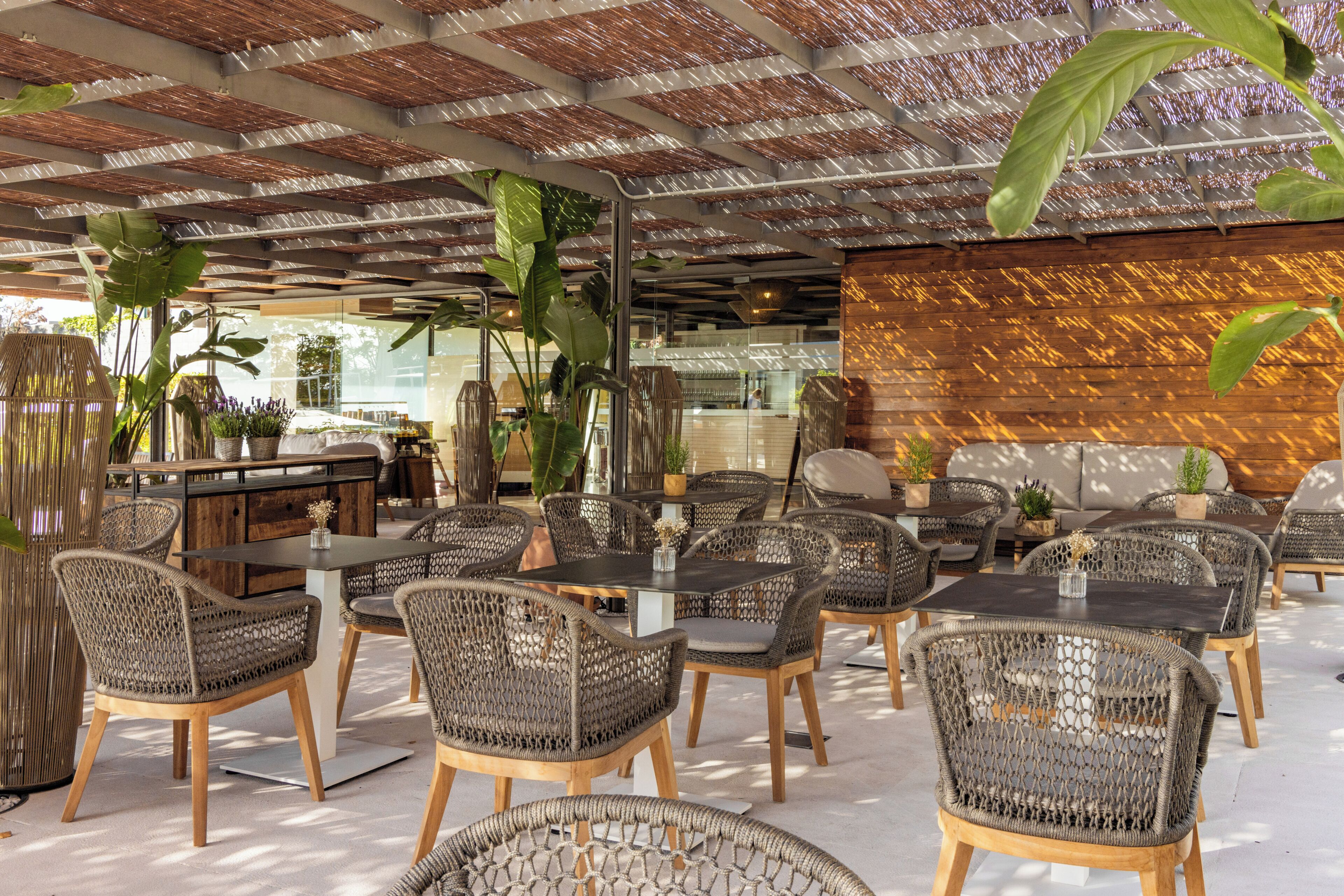 An outdoor seating area with wicker chairs and tables, a wooden wall, and potted plants.